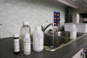 A decorative photo of sample bottles next to a sink with the tap running.